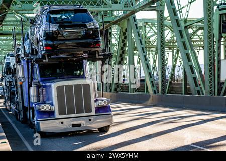 Industrial carrier long car hauler blue big rig semi truck tractor transporting cars on two level hydraulic semi trailer running on the truss metal ar Stock Photo