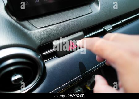 The hazard or emergency light button is pressed by the driver hand. Automotive concept Stock Photo