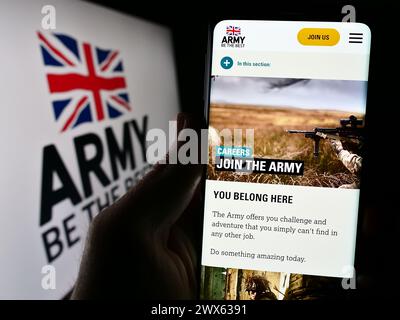 Person holding cellphone with webpage of United Kingdom ground force British Army in front of logo. Focus on center of phone display. Stock Photo