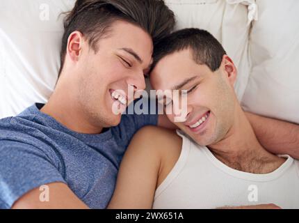 Men, gay and happy couple or bed embrace in apartment resting for lgbt pride with relax love, partner or connection. Male person, queer and smile with Stock Photo