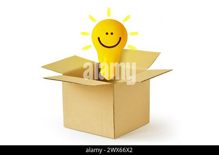 Yellow light bulb with smile in cardboard box - Concept of ideas and creativity Stock Photo