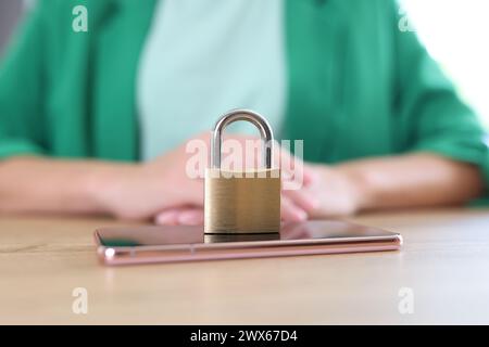 Metal padlock and mobile phone on wooden table close-up, woman in background. Stock Photo