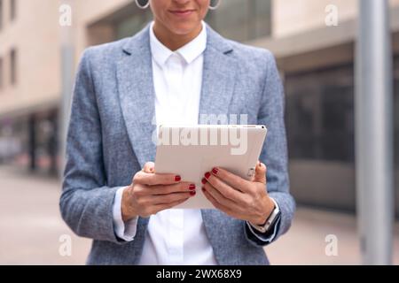 Unrecognizable Caucasian business woman with pensive face using a digital tablet outdoors. Stock Photo