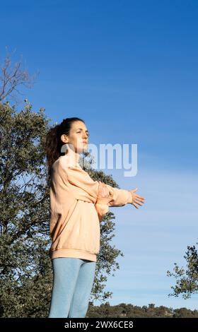 Woman stretching shoulders after exercising in nature dressed in peach color Stock Photo