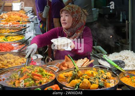 London, UK - 12 September, 2023 - A asian muslim female serving curry takeaway at Camden street food market Stock Photo