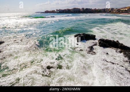 sozopol, bulgaria - 09 aug 2015: cityscape of the old town at the sea. waves crashing on the rocky coast in morning light. beautiful travel destinatio Stock Photo