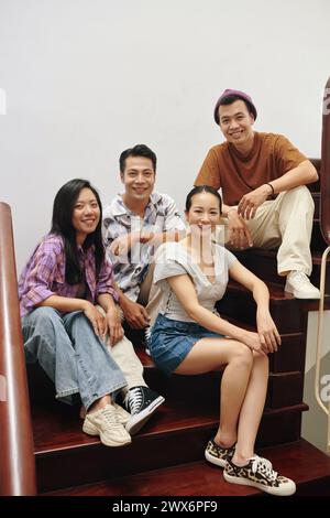 Smiling Vietnamese young people sitting on wooden steps at home Stock Photo