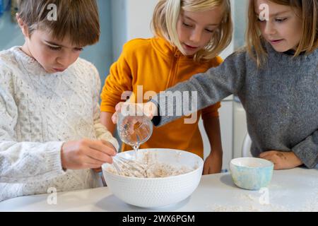 Three children preparing a homemade pizza dough together Stock Photo