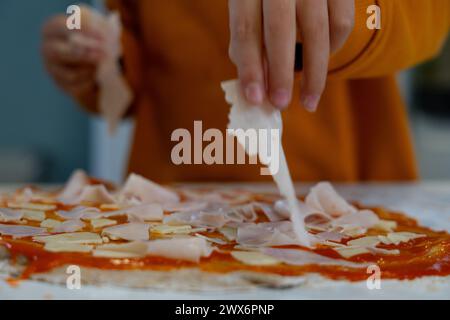 Child's hands cooking homemade pizza putting the ingredients on the dough Stock Photo