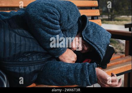 homeless elderly old Caucasian man lies sleeping on a park bench in autumn Stock Photo