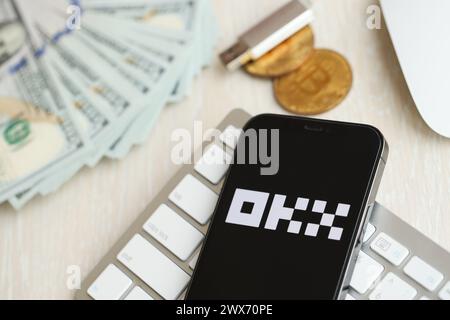 KYIV, UKRAINE - MARCH 15, 2024 OKX logo on iPhone display screen on white keyboard with money and bitcoins. Cryptocurrency exchange portal Stock Photo