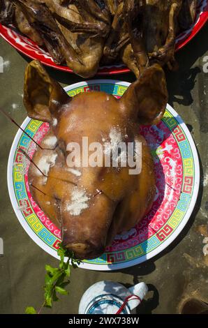 Big cooked pig head on plate on table among other dishes offerings to God at Chinese New Year in Koh Tao island, Thailand Stock Photo