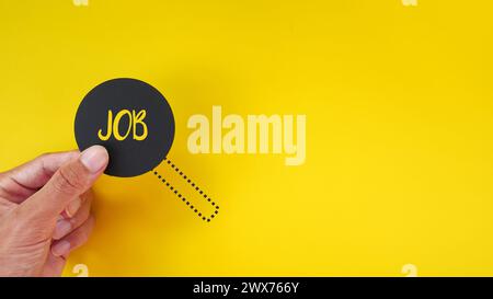 Hand holding a magnifying glass with the word JOB. Minimalist background of job vacancy concept. Searching job. Stock Photo