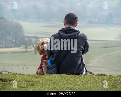 One man and his cute Cockapoo dog looking at camera sitting on hilltop, Leicestershire, UK Stock Photo
