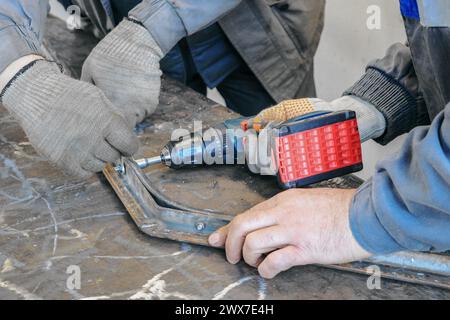A worker on a construction site operates a drill to cut through a metal profile, demonstrating precision and efficiency in metalworking tasks. Stock Photo