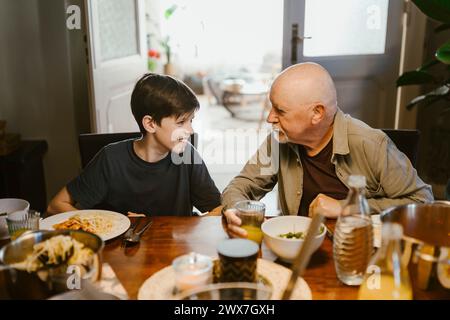 Senior man talking with grandson while sitting at dining table in home Stock Photo