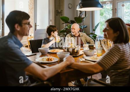 Grandfather and grandson having juice while sitting with family at dining table in home Stock Photo