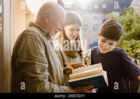 Side view of senior man reading book to grandchildren in balcony Stock Photo
