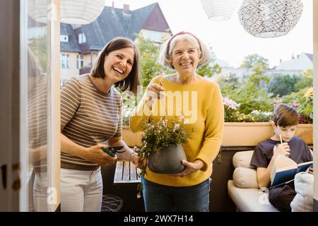 Happy woman and mother-in-law holding potted plant in balcony Stock Photo