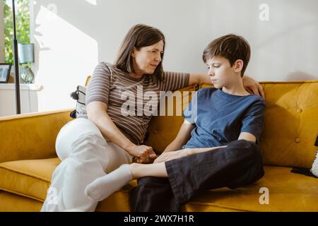 Serious woman consoling son while sitting on sofa at home Stock Photo