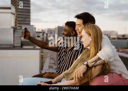 Young man taking selfie with friends through smart phone while sitting on terrace Stock Photo