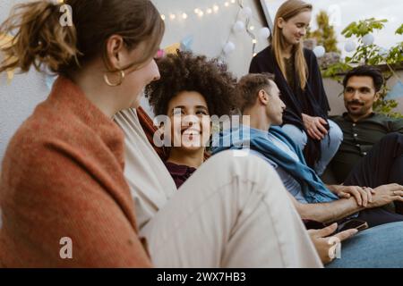 Smiling woman talking with female friends while sitting at party in balcony Stock Photo