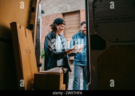 Male and female delivery coworkers sorting out parcels while standing near van Stock Photo