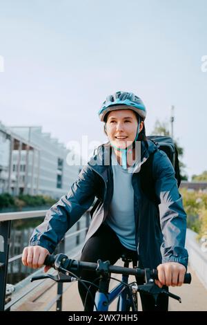 Smiling female delivery person wearing helmet and sitting on bicycle Stock Photo