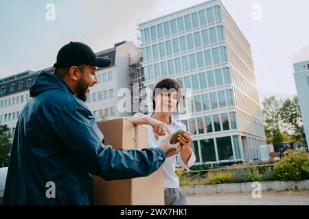 Mature woman doing digital signature while receiving parcel from male delivery person in front of building Stock Photo