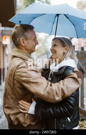 Side view of romantic mature couple standing under umbrella at street Stock Photo