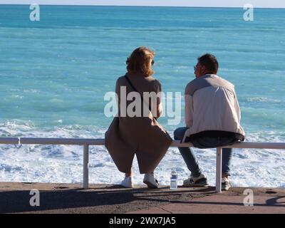 Romance in the French Riviera: a young couple perch on the railings on the Promenade des Anglais in Nice, gazing out to sea. Stock Photo