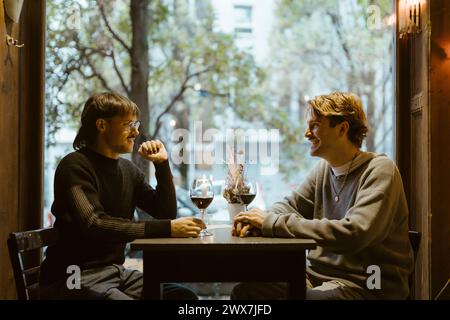 Happy gay couple talking while sitting with wineglasses on table during date at restaurant Stock Photo