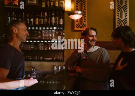 Male bartender looking at gay couple enjoying drinks at bar Stock Photo