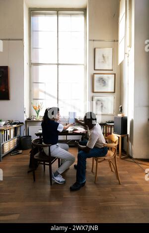 Male and female colleagues discussing over document while sitting on chair Stock Photo