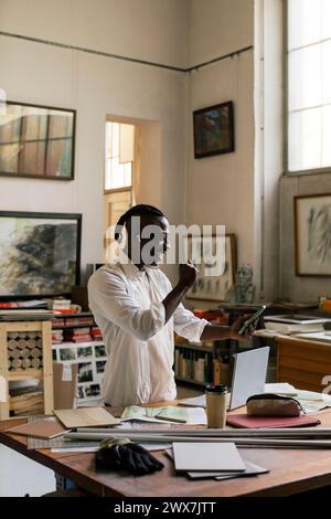 Smiling businessman clenching fist and using smart phone while standing in workshop Stock Photo