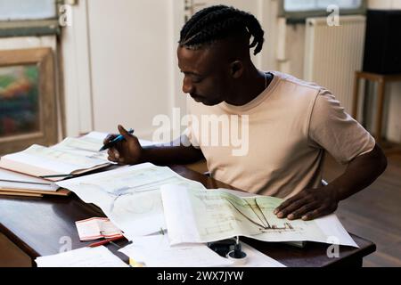 Focused male architect analyzing blueprints at table in workplace Stock Photo