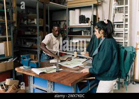 Male architect showing metal rods to female customer in workshop Stock Photo