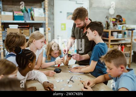 Male teacher helping students while working on robotics project at workshop in school Stock Photo