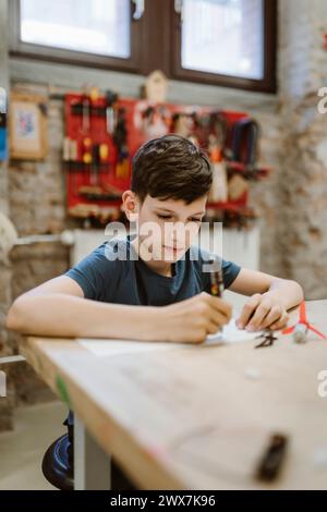 Male student working on robotics project while sitting at table in workshop Stock Photo