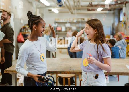 Cheerful female students giving high-five while standing near table in classroom Stock Photo
