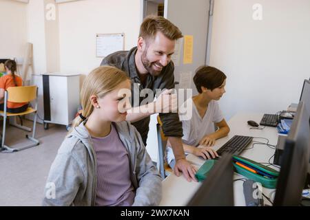 Smiling male teacher assisting female student using computer in classroom at school Stock Photo
