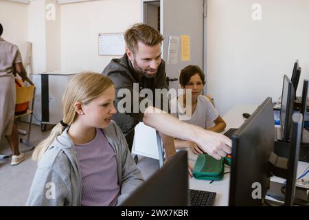 Male teacher pointing at monitor while explaining female student in classroom at school Stock Photo