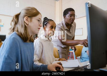 Female teacher explaining students over computer in classroom at school Stock Photo