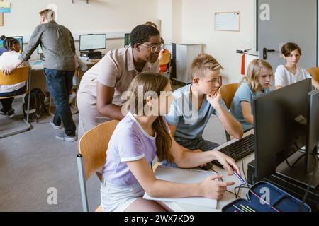 Male and female teacher assisting students in computer class at school Stock Photo