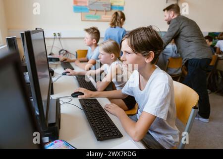 Concentrated male pupil using computer while sitting with students at desk in computer classroom Stock Photo