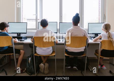 Rear view of male and female students using computers while sitting in classroom at school Stock Photo