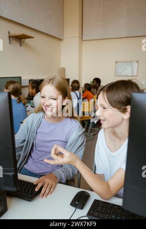 Smiling boy talking to female friend using computer while sitting in classroom at school Stock Photo