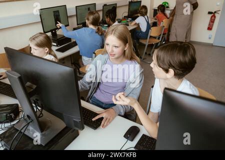 High angle view of male and female classmates discussing while sitting in computer class at school Stock Photo