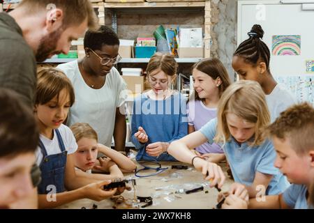 Group of students and teacher assisting each other while working on robotics project at workshop in school Stock Photo