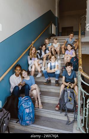 Portrait of smiling multiracial male and female students sitting on school staircase Stock Photo